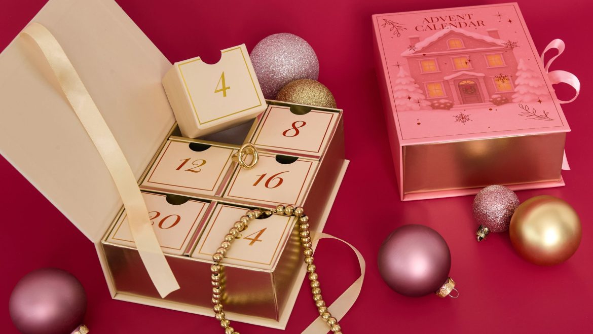 A luxury pink-and-gold Christmas advent calendar (with numbered compartments) containing jewelry, paired with glittery Christmas baubles.